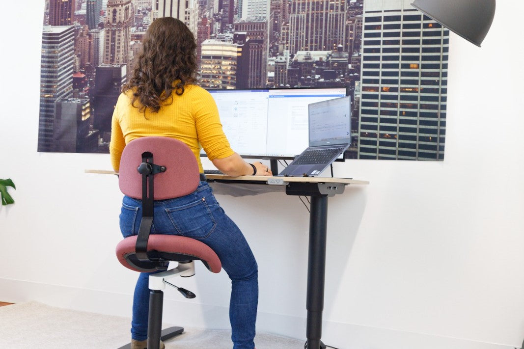 Person auf aktiv-dynamischen Sattelstuhl Aurelia am Schreibtisch sitzend